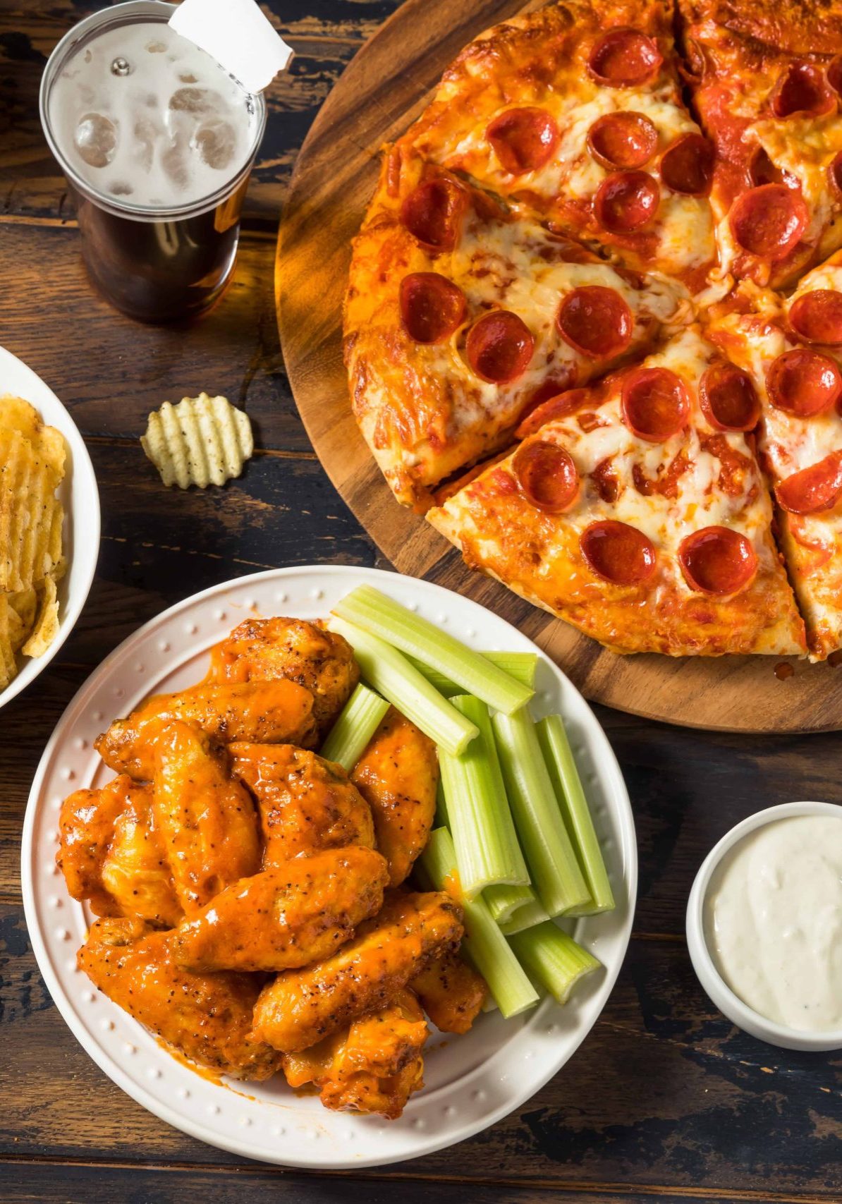 Pizza, wings, celery and chips on a wooden table.